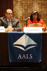 Paulette Brown in orange, wearing glasses seated behind table with AALS banner on right with Richard A. Matasar on left